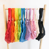 Set of colorful mesh bags on a wooden rack against a white background