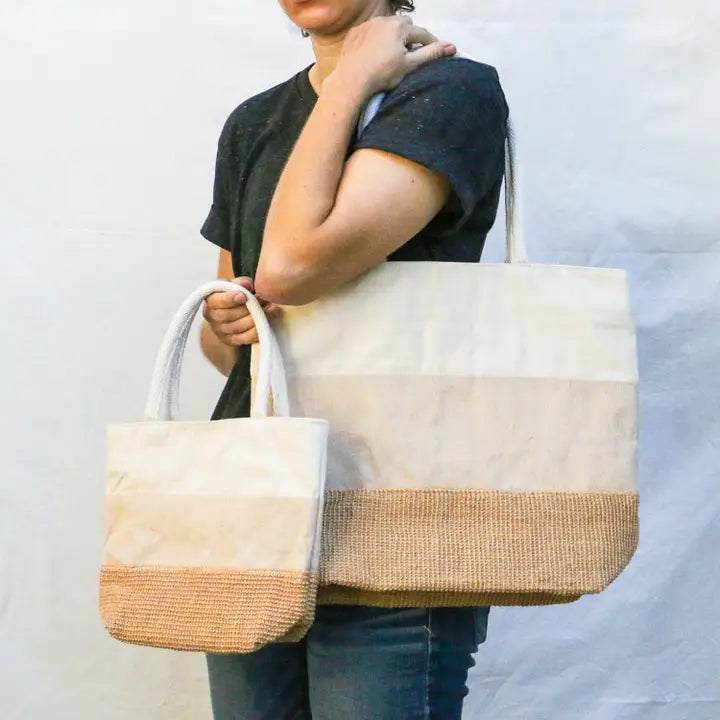 A person in a dark shirt and jeans holds two Simple Ecology Tricolor Cotton &amp; Jute Shoulder Bags—one large, one small—against a plain light background.