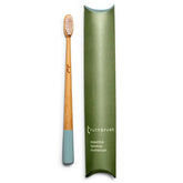 A Truthbrush - Bamboo Toothbrush with light blue bristles and tip lies next to its green, rectangular packaging labeled "Truthbrush beautiful bamboo toothbrush.