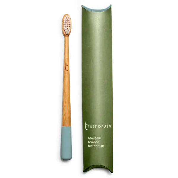 A Truthbrush - Bamboo Toothbrush with light blue bristles and tip lies next to its green, rectangular packaging labeled "Truthbrush beautiful bamboo toothbrush.