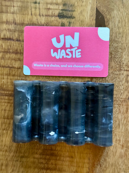 An Upcycled Soap Tray from Unwaste, featuring a pink card that reads “Waste is a choice, and we choose differently,” is displayed on a wooden surface, inspiring a zero-waste bathroom lifestyle.