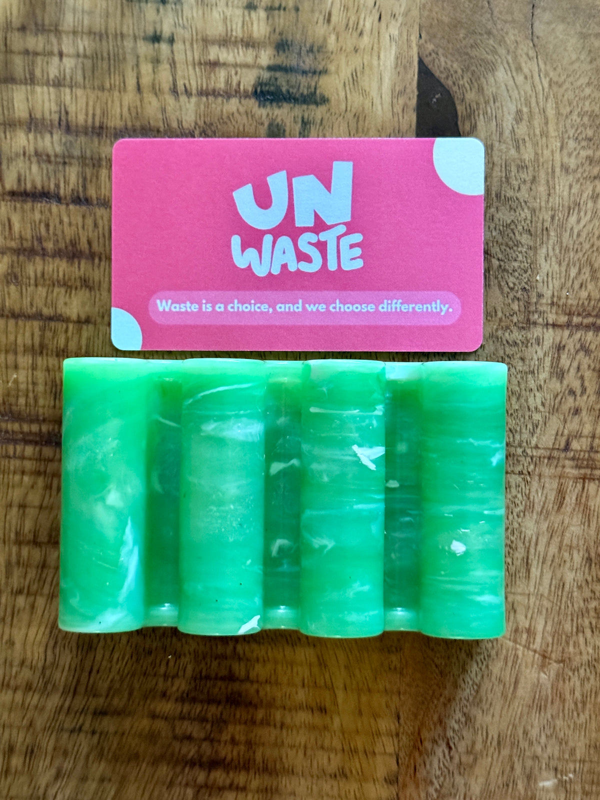 An Upcycled Soap Tray from Unwaste holds a green soap bar and a pink card emblazoned with “Waste is a choice, and we choose differently.” Together, they create an inspiring scene for any zero-waste bathroom.