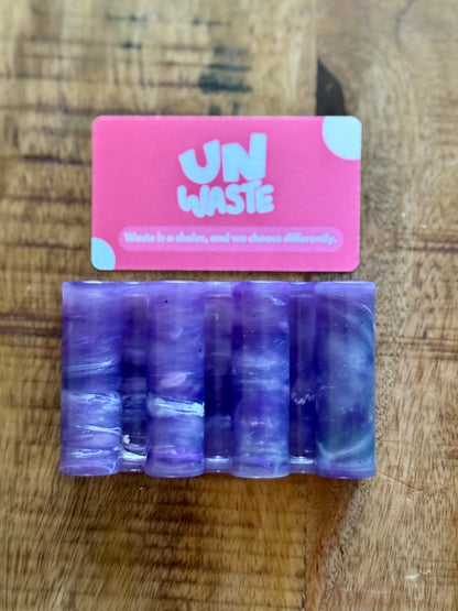 An Upcycled Soap Tray by Unwaste sits above five purple cylindrical objects on a wooden surface, providing a stylish and sustainable touch to your zero-waste bathroom.