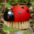 The Zefiro Ladybug Brush features natural sisal bristles and a red-and-black ladybug handle, offering an eco-friendly, plastic-free cleaning solution that looks great among green plants outdoors.