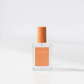 A clear glass bottle of BKind Nail Polish with an orange label and matching orange cap is displayed against a white background with soft shadows. The label features the BKind brand, recognized for plant-based nail polish.