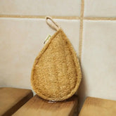 The Bamboo Switch Loofah is a tear-shaped natural sponge with a hanging loop, shown against beige tiles and wooden slats—an eco-friendly exfoliator ideal for your daily routine.
