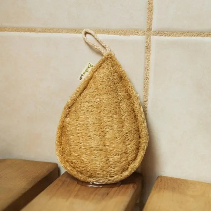 The Bamboo Switch Loofah is a tear-shaped natural sponge with a hanging loop, shown against beige tiles and wooden slats—an eco-friendly exfoliator ideal for your daily routine.