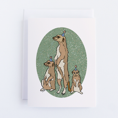 Eco-conscious Greeting Cards from Bean Horse Car Designs feature Kate Pinto’s illustration of three meerkats in blue party hats before a green, white-speckled oval.