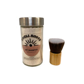 A glass jar of Swell Roots Dry Shampoo with a metal lid is placed beside a short, wide makeup brush featuring a bamboo handle and soft bristles, both displayed against a white background.