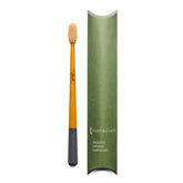 A Truthbrush - Bamboo Toothbrush with a gray tip is shown beside its green, rectangular packaging labeled “Truthbrush beautiful bamboo toothbrush.”.