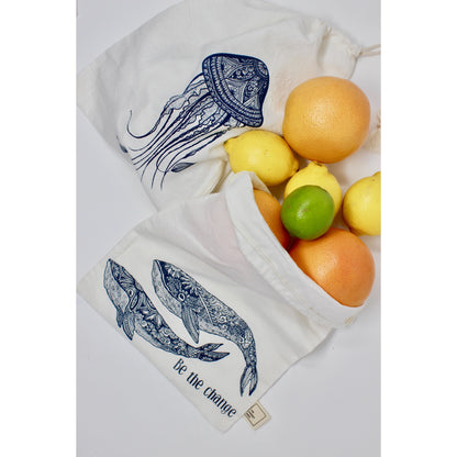 Two Your Green Kitchen Reusable Cotton Bags, handmade in Canada and decorated with blue jellyfish and whale designs reading “Be the change,” hold grapefruits, lemons, and a lime on a white surface.